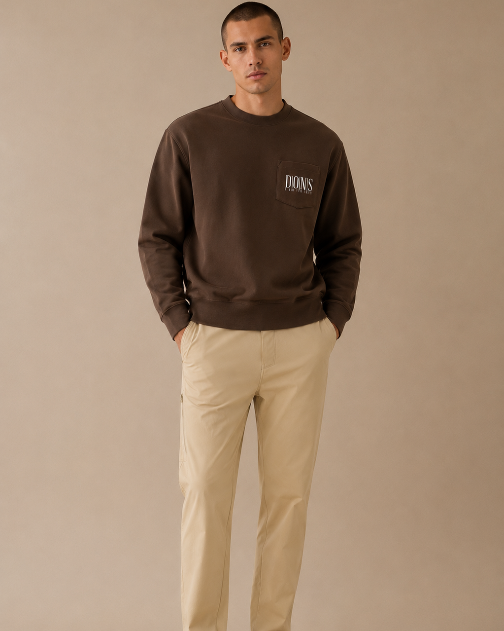 Man wearing a brown sweatshirt with a logo and beige pants on a beige background