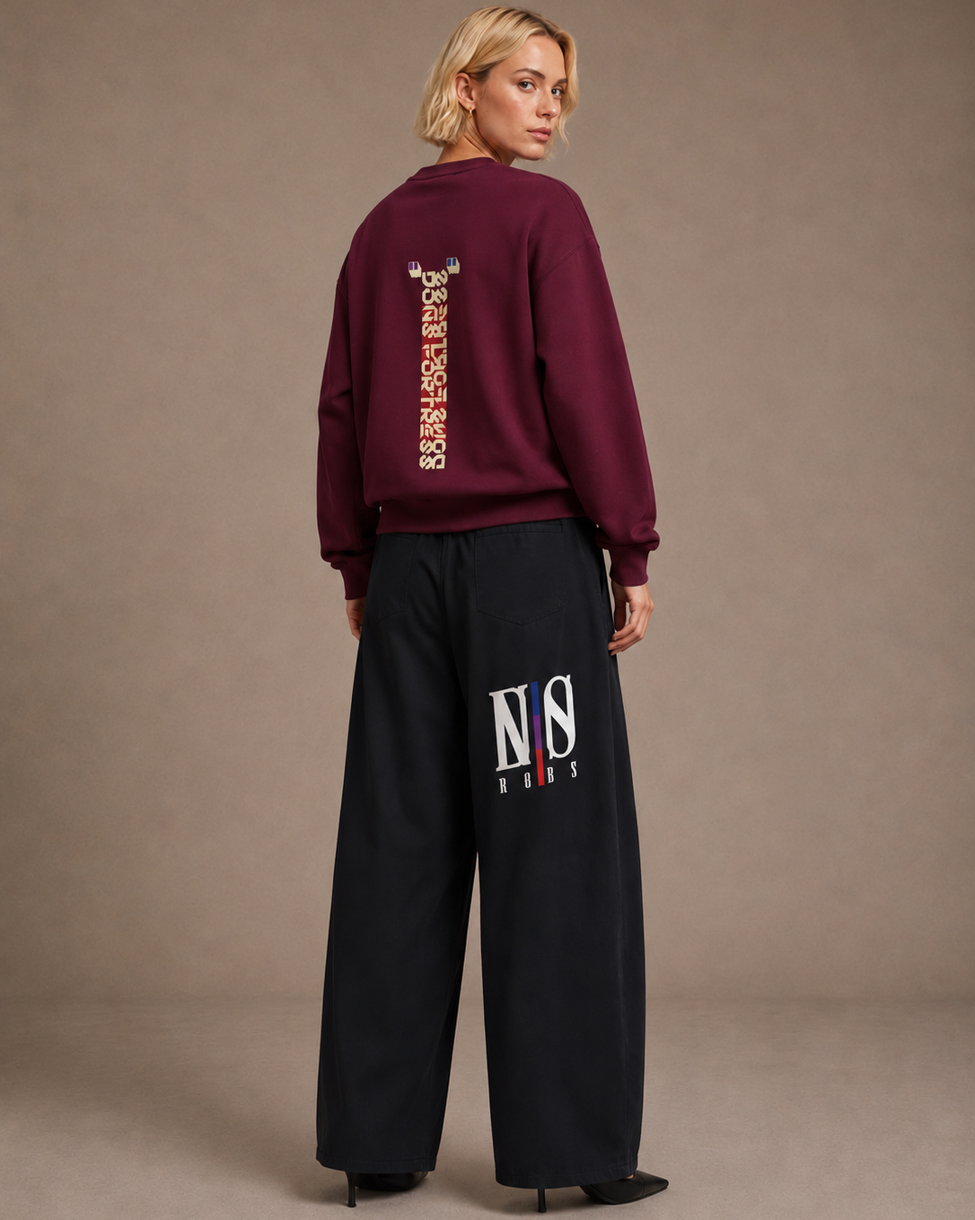 Person wearing a burgundy sweatshirt and black pants with visible branding on a beige background