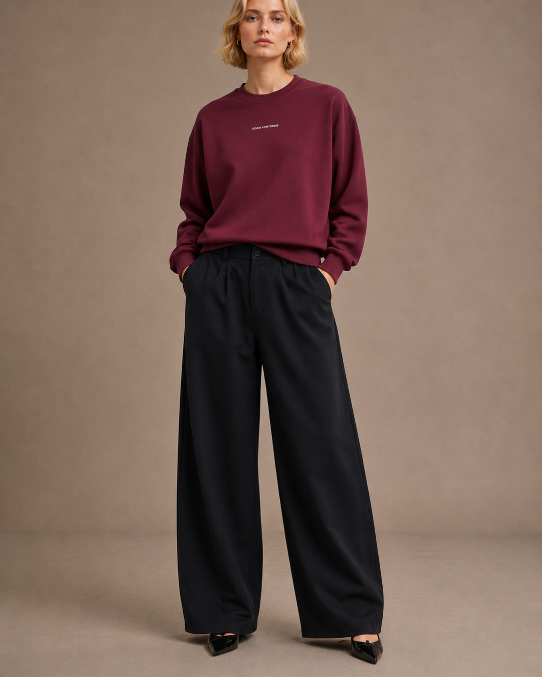 Person wearing a burgundy sweater and black pants against a beige background