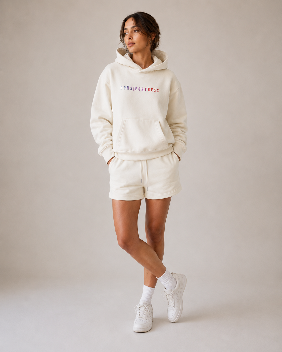 Woman wearing a cream-coloured hoodie and shorts set with text on the hoodie against a plain background