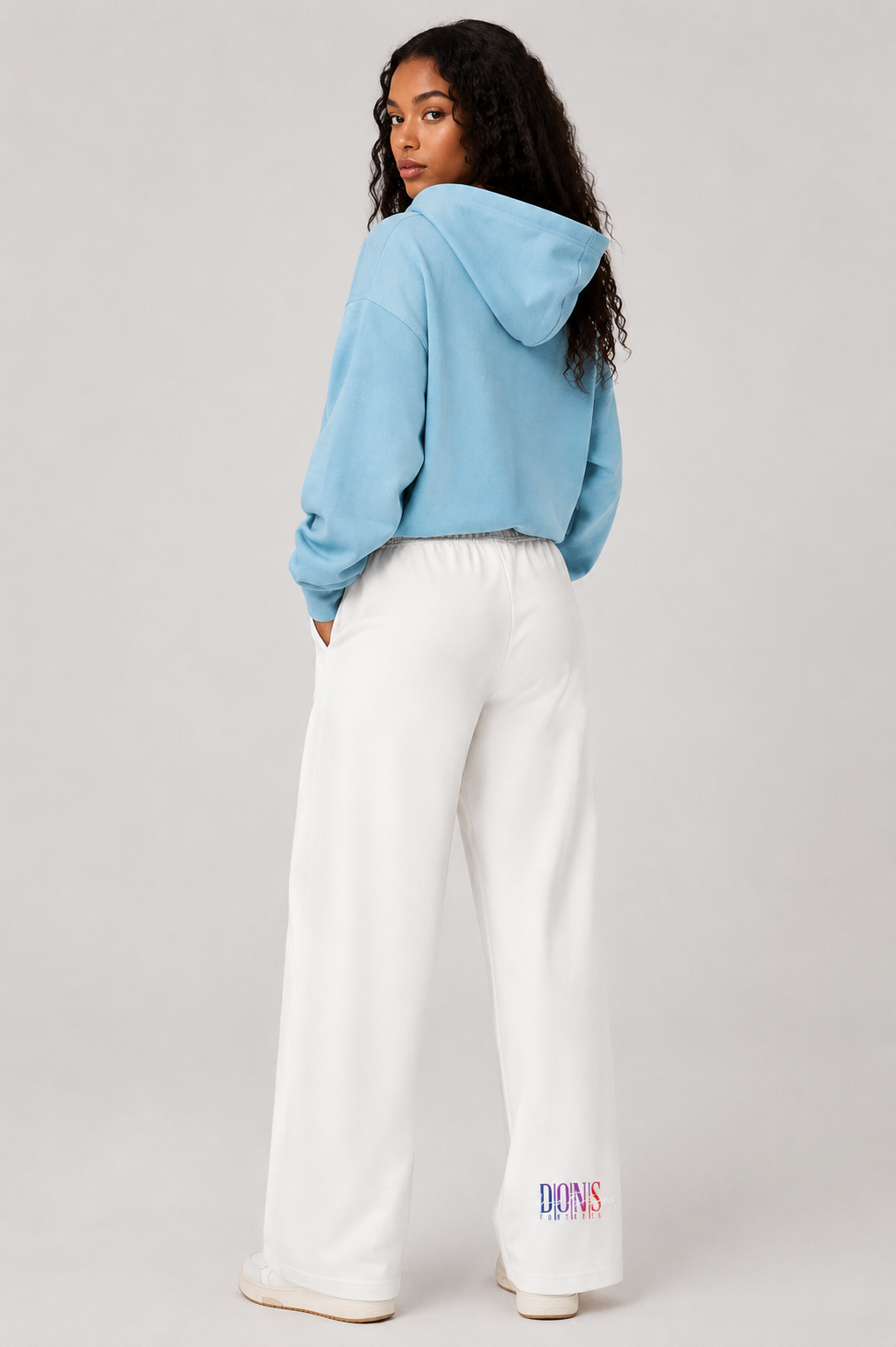 Person wearing a light blue hoodie and white pants on a plain background