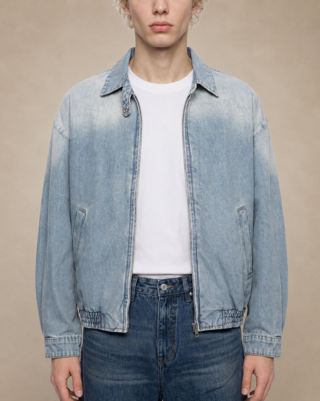 Person wearing a light blue denim jacket over a white shirt and dark jeans on a beige background